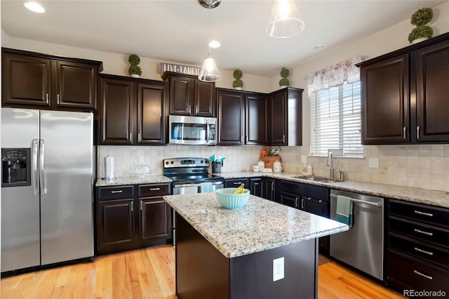 kitchen with light wood finished floors, a sink, stainless steel appliances, pendant lighting, and a center island