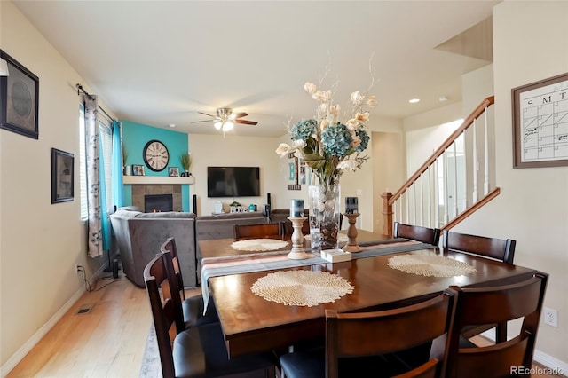 dining space featuring baseboards, light wood-style floors, ceiling fan, and stairs