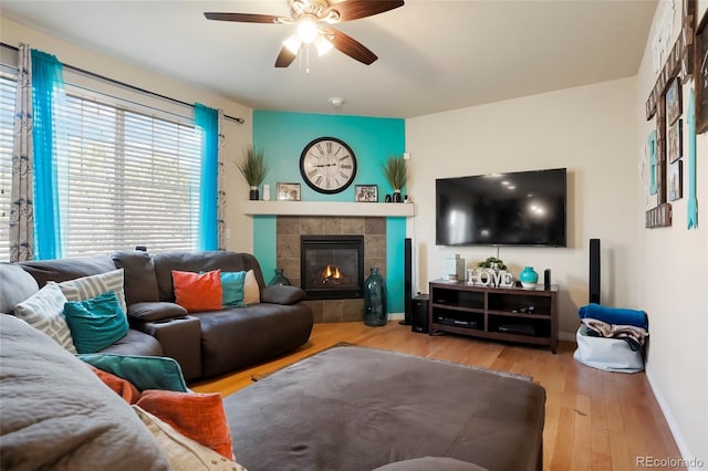 living room featuring ceiling fan, a fireplace, baseboards, and wood finished floors