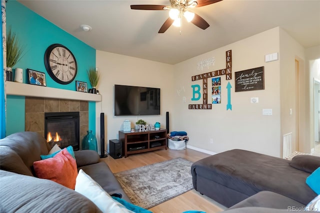 living area featuring a tiled fireplace, wood finished floors, visible vents, and a ceiling fan