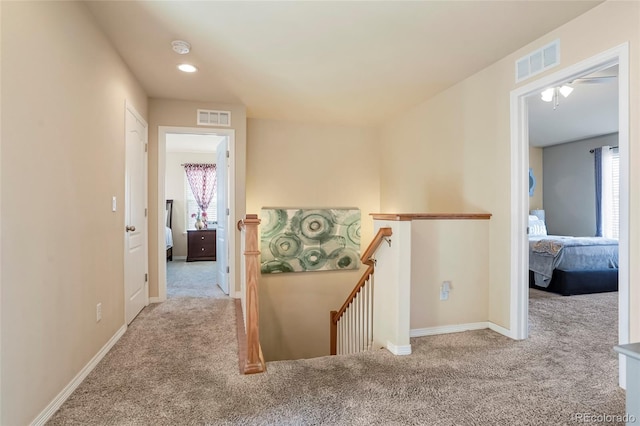 hall featuring an upstairs landing, visible vents, baseboards, and carpet floors