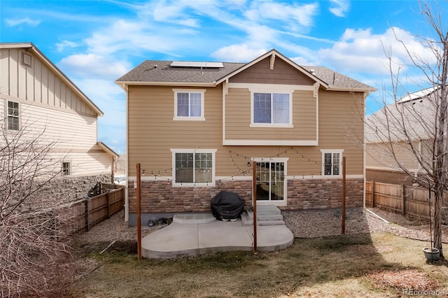 rear view of property with solar panels, a patio, a fenced backyard, and stone siding