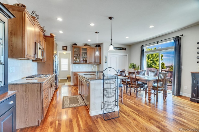 kitchen with stainless steel appliances, tasteful backsplash, hanging light fixtures, light stone counters, and sink