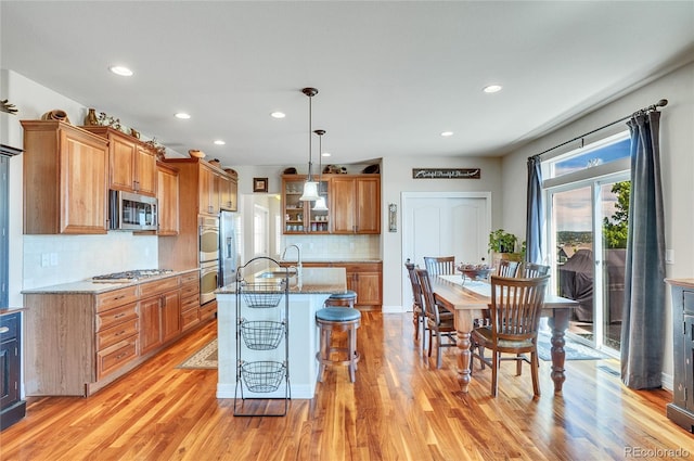 kitchen with appliances with stainless steel finishes, an island with sink, light stone counters, and decorative light fixtures