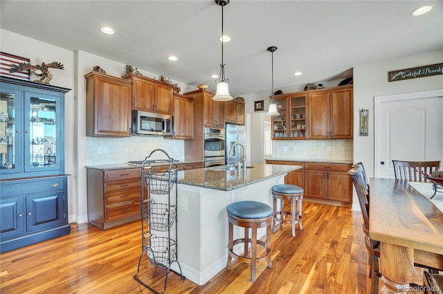 kitchen with tasteful backsplash, dark stone countertops, a center island with sink, hanging light fixtures, and appliances with stainless steel finishes