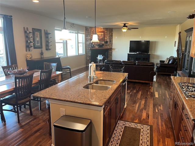 kitchen featuring ceiling fan, pendant lighting, sink, an island with sink, and a stone fireplace