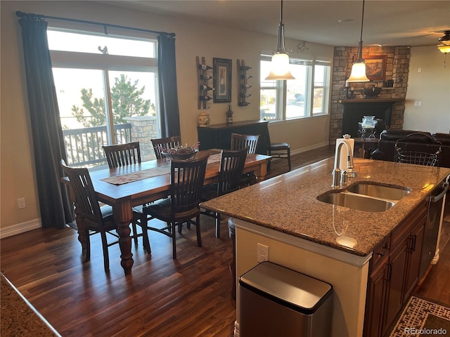 kitchen featuring a fireplace, pendant lighting, sink, dark wood-type flooring, and light stone counters