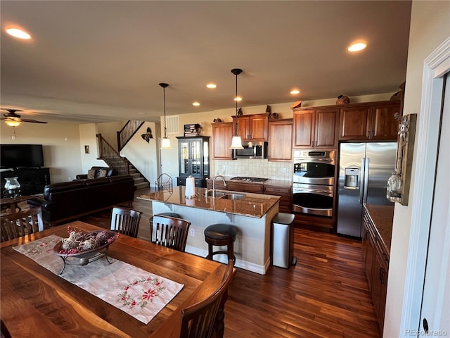 kitchen featuring an island with sink, a breakfast bar area, stainless steel appliances, tasteful backsplash, and decorative light fixtures