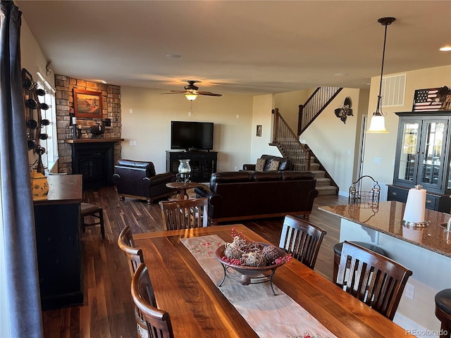 dining space featuring ceiling fan, dark hardwood / wood-style floors, and a stone fireplace