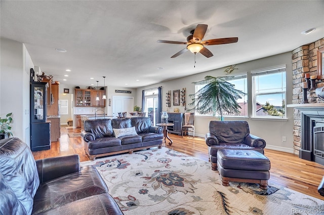 living room with ceiling fan, a fireplace, sink, and light hardwood / wood-style floors