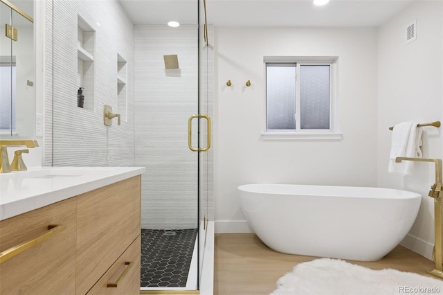 bathroom with wood finished floors, visible vents, vanity, a freestanding bath, and a stall shower