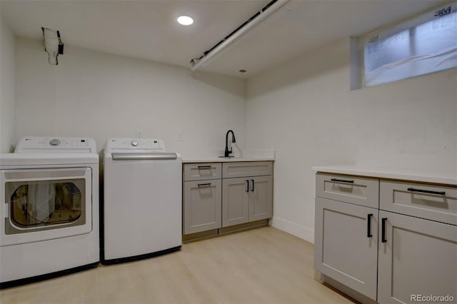 washroom featuring light wood-style flooring, a sink, baseboards, independent washer and dryer, and cabinet space