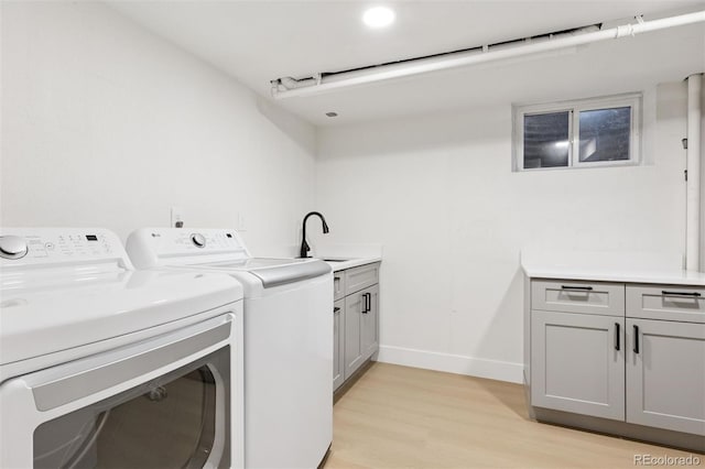 laundry room with a sink, baseboards, washer and dryer, cabinet space, and light wood finished floors