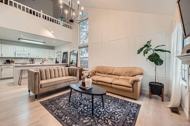 living room featuring a high ceiling, a chandelier, visible vents, and light wood-style floors