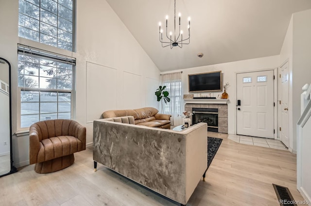 living area featuring visible vents, a fireplace, high vaulted ceiling, light wood-type flooring, and a notable chandelier