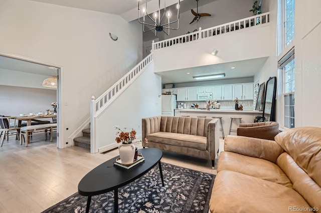 living room with stairs, high vaulted ceiling, a notable chandelier, and light wood-type flooring