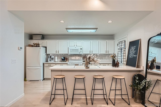 kitchen with a peninsula, a breakfast bar area, white appliances, and light wood-style flooring