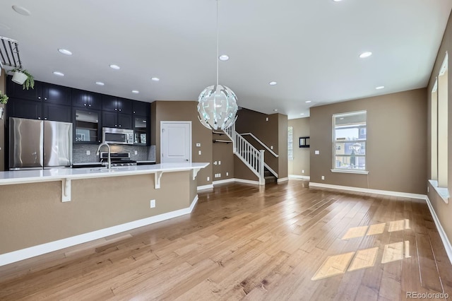 11323 Uptown Ave, Broomfield, CO 80021 - kitchen featuring light wood finished floors, a kitchen breakfast bar, dark cabinets, light countertops, and appliances with stainless steel finishes