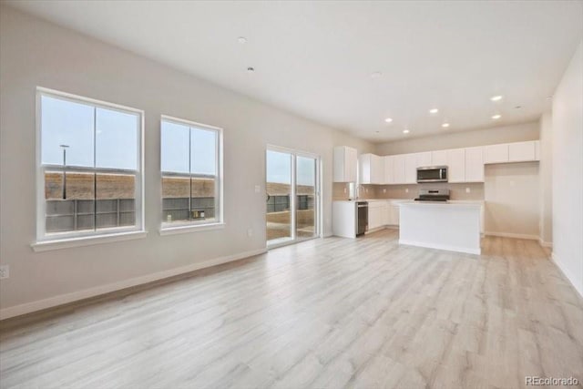 unfurnished living room with baseboards, recessed lighting, light wood-type flooring, and a sink