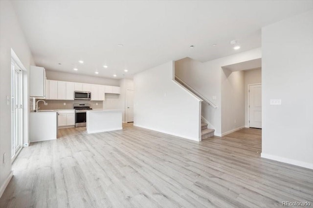 unfurnished living room featuring light wood-type flooring, baseboards, a sink, and recessed lighting