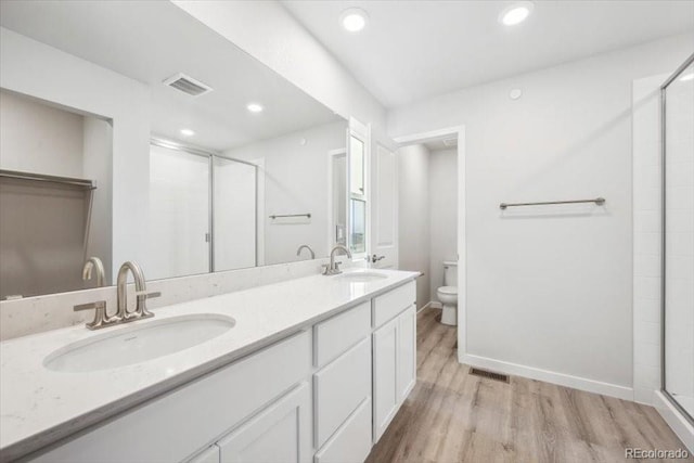 bathroom featuring toilet, wood finished floors, a shower stall, and a sink