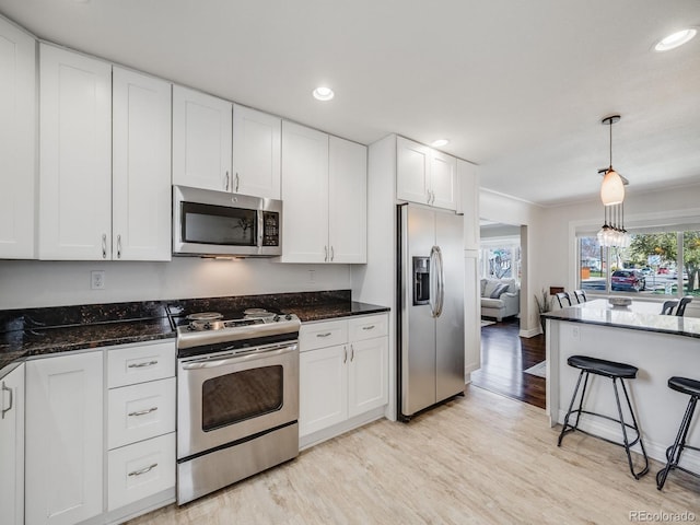 kitchen featuring dark stone counters, stainless steel appliances, light wood-type flooring, and white cabinetry