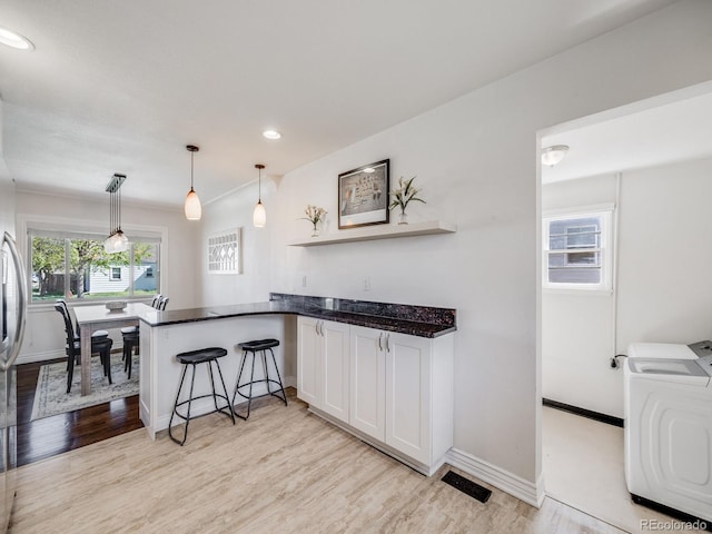 kitchen featuring white cabinets, light wood-style floors, washer / clothes dryer, a peninsula, and a kitchen bar