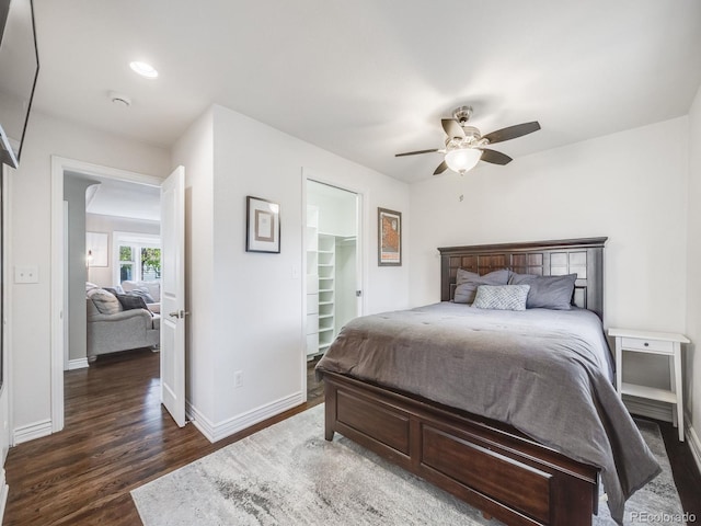 bedroom featuring dark wood-style flooring, baseboards, a spacious closet, and ceiling fan