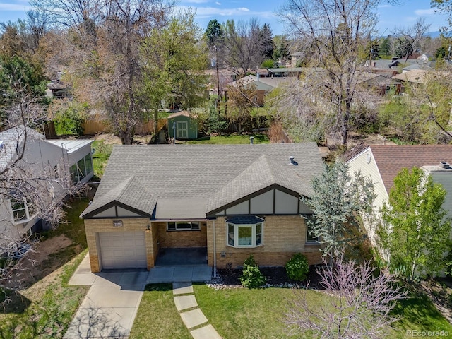 view of front of home featuring a shingled roof, brick siding, a storage shed, a garage, and driveway