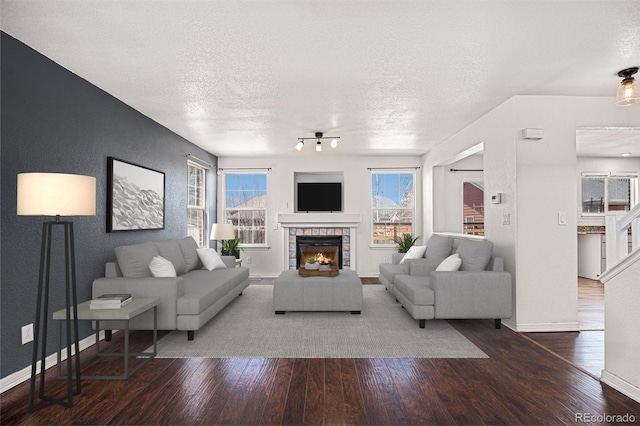 living area featuring wood finished floors, a textured ceiling, baseboards, a fireplace, and plenty of natural light