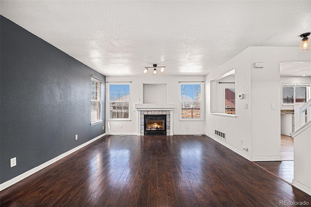 unfurnished living room featuring wood finished floors, baseboards, a textured ceiling, a textured wall, and a tile fireplace
