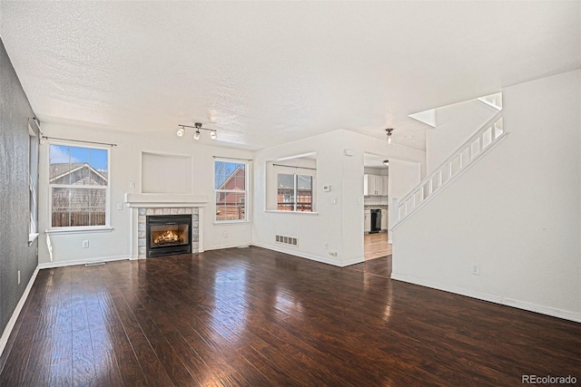 unfurnished living room featuring a tile fireplace, hardwood / wood-style flooring, healthy amount of natural light, baseboards, and a textured ceiling