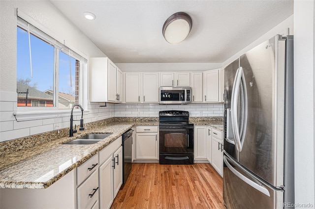 kitchen featuring black appliances, a sink, light wood finished floors, and tasteful backsplash