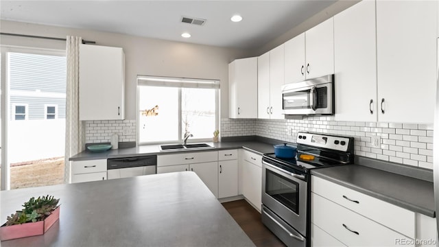 kitchen with a sink, stainless steel appliances, dark countertops, and visible vents