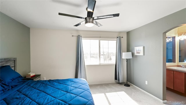 bedroom featuring light carpet, ensuite bathroom, a sink, arched walkways, and baseboards