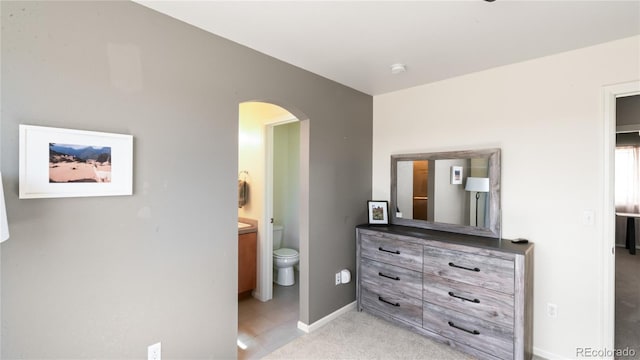 bedroom featuring arched walkways, light colored carpet, connected bathroom, and baseboards