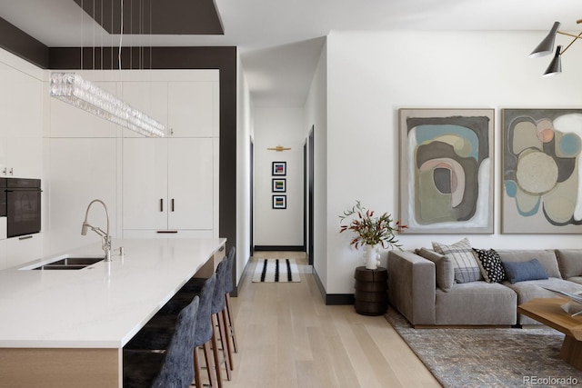 interior space with sink, oven, white cabinets, and light wood-type flooring