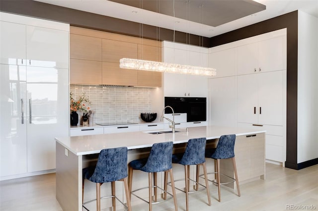 kitchen featuring sink, a breakfast bar area, a large island with sink, wall oven, and decorative backsplash