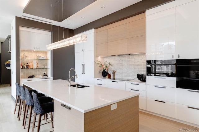 kitchen with a breakfast bar, sink, white cabinets, black appliances, and a center island with sink