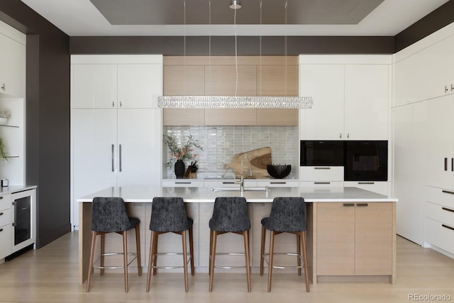 kitchen with a kitchen bar, a kitchen island with sink, and white cabinets