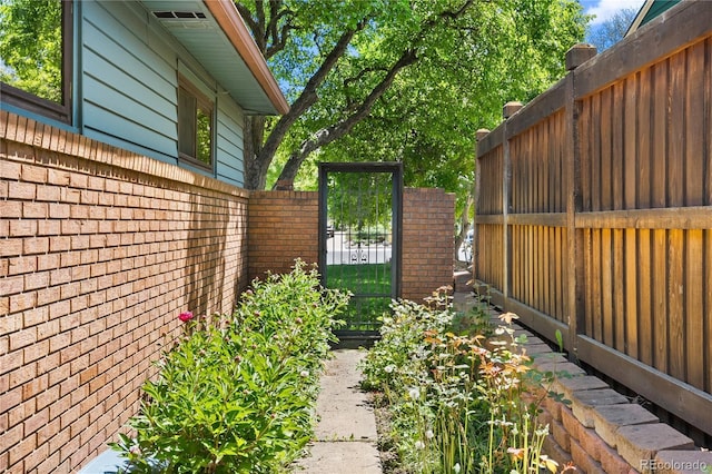 view of property exterior featuring brick siding, fence, and a gate