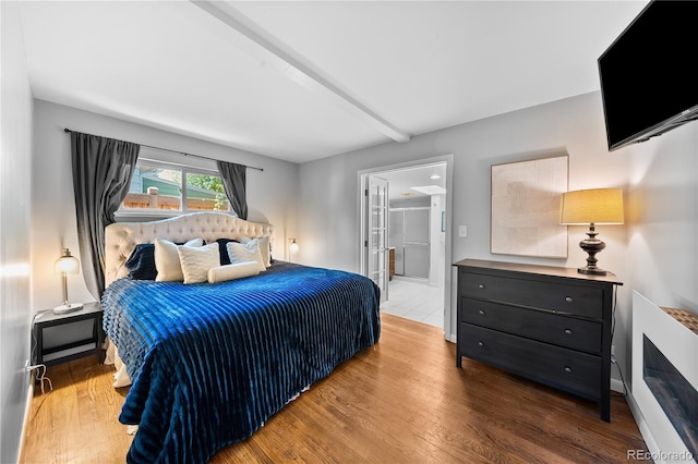 bedroom featuring wood finished floors, beamed ceiling, and ensuite bathroom