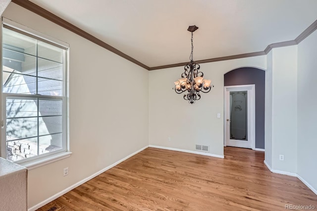 spare room featuring visible vents, ornamental molding, arched walkways, light wood-style floors, and an inviting chandelier