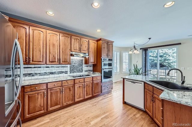 kitchen featuring brown cabinets, light wood-style flooring, a sink, under cabinet range hood, and appliances with stainless steel finishes