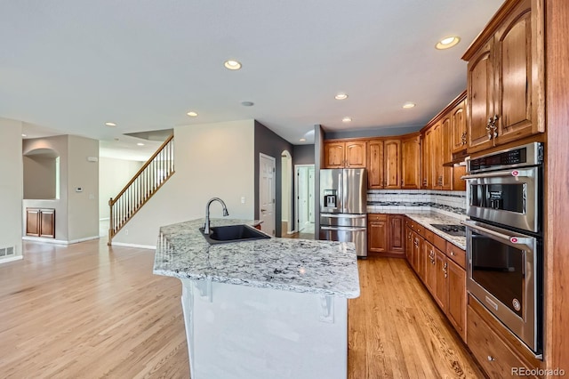 kitchen with a sink, appliances with stainless steel finishes, light wood-style flooring, and a center island with sink