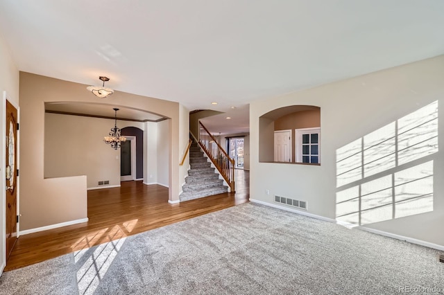 carpeted spare room featuring visible vents, baseboards, an inviting chandelier, arched walkways, and stairs