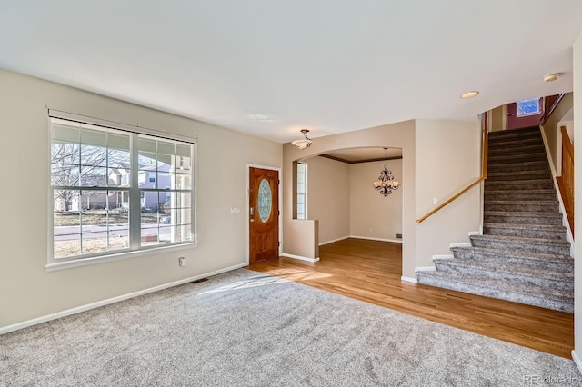 carpeted foyer with baseboards, stairs, an inviting chandelier, and wood finished floors