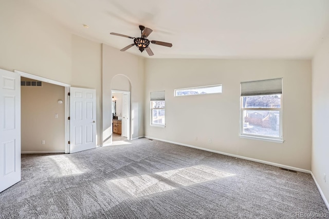 unfurnished bedroom featuring visible vents, baseboards, arched walkways, carpet flooring, and connected bathroom