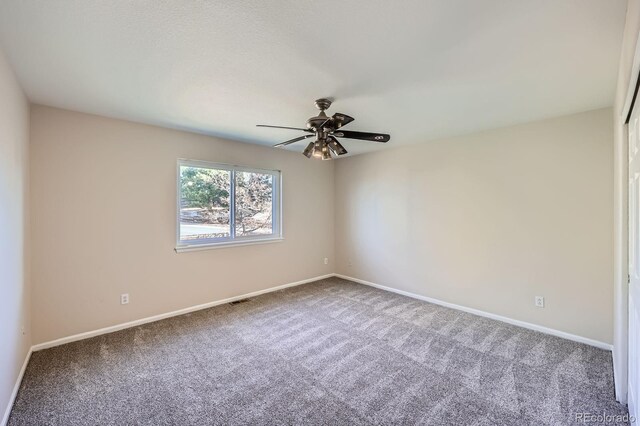 carpeted spare room with visible vents, baseboards, and ceiling fan