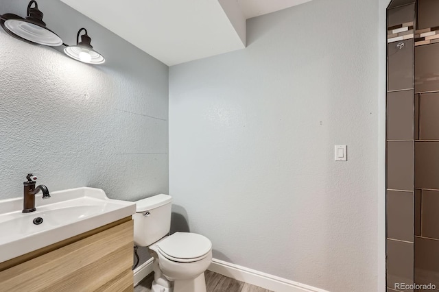 bathroom with vanity, wood finished floors, baseboards, toilet, and a textured wall